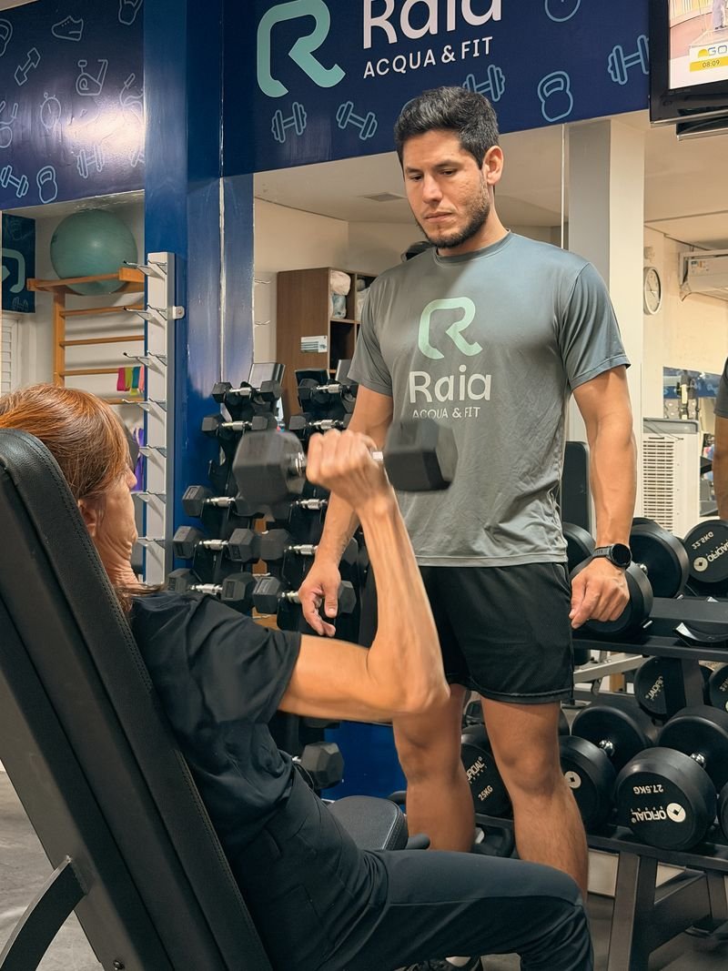 Professor da Raia Acqua & Fit acompanhando uma aluna durante exercício com halter
